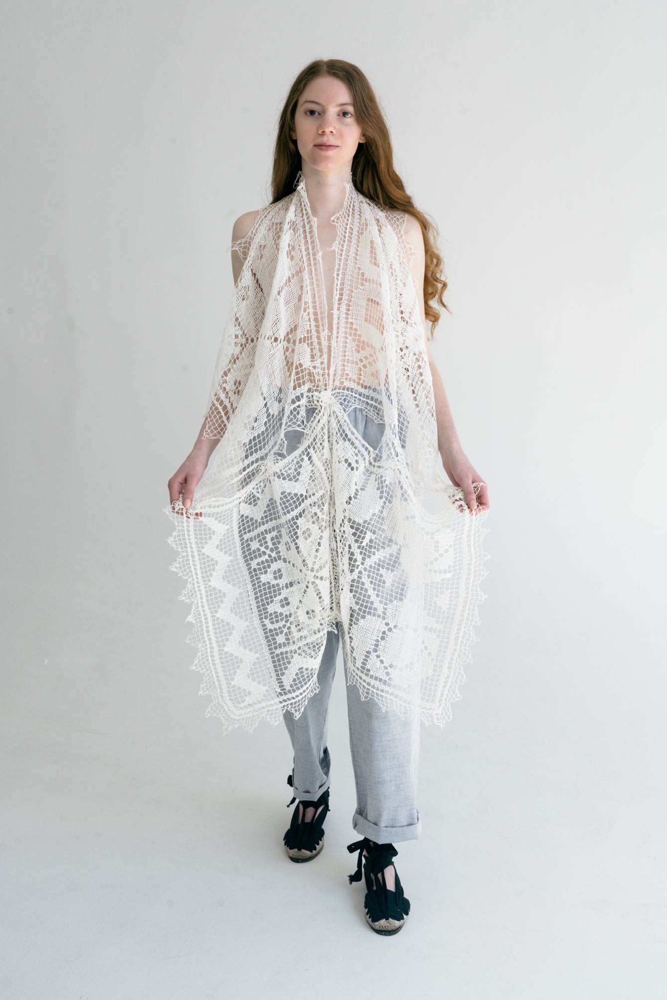 A woman standing in a studio setting, wearing a white, hand-loomed cotton lace top with long sleeves.